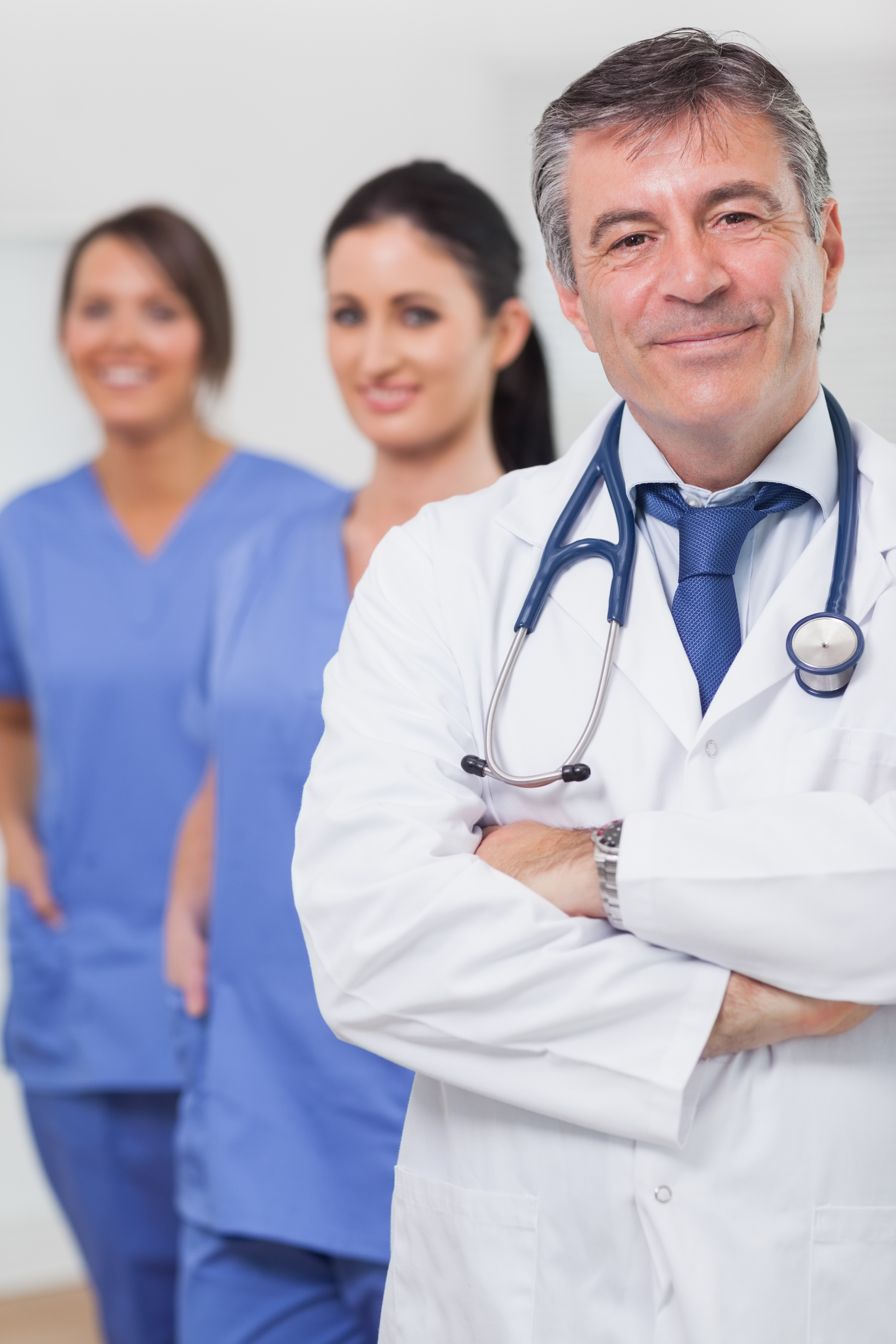 Doctor with arms crossed and his team of nurses smiling 300x400